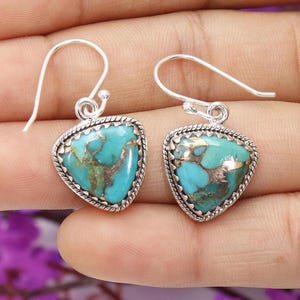 May include: A pair of silver-toned earrings with turquoise-colored, heart-shaped stones. The stones have a copper-colored matrix and are framed by a twisted rope design. The earrings have a simple hook closure.