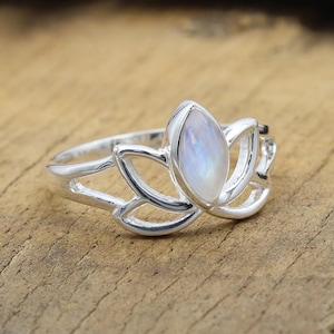 May include: A silver ring with a teardrop-shaped, iridescent gemstone set in a lotus flower design. The ring's band and lotus petals are made of polished silver, creating a delicate and elegant piece of jewellery.