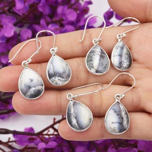 May include: A pair of silver dangle earrings with teardrop-shaped dendritic opal stones. The stones are a mix of white and gray with black dendritic patterns.