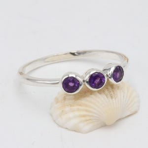 May include: A silver ring with three round amethyst gemstones set in a row.