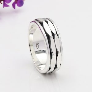 May include: A silver ring with a textured, repeating leaf-like pattern around the band. The ring is marked with "925" on the inside, indicating its silver content. The ring is displayed on a white surface.