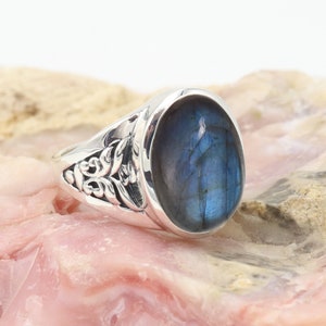 May include: A silver ring featuring an oval blue labradorite gemstone. The ring band has a floral design.