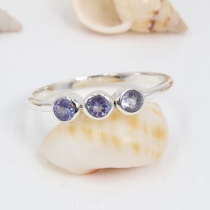 May include: A silver ring with three round, purple gemstones set in a row.