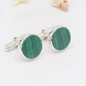 May include: A pair of silver cufflinks with round green malachite stone insets.
