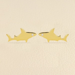May include: A pair of gold shark earrings with a small diamond accent on each shark.