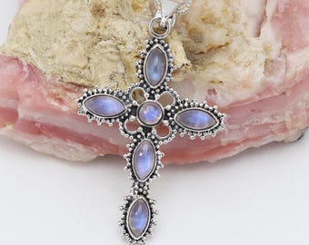 May include: Silver cross pendant with a delicate design and six moonstone gemstones. The pendant is set against a pink and white background.