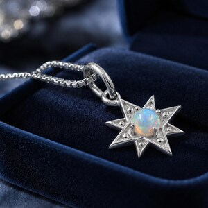 May include: A silver-toned star-shaped pendant necklace featuring a central round iridescent opal gemstone. The star design includes small raised metal dots on each point and is attached to a delicate box chain, creating a detailed jewelry piece.