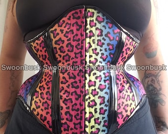 May include: A rainbow leopard print corset with black boning and a black zipper in the back. The corset is made of a shiny fabric and has a glossy finish.