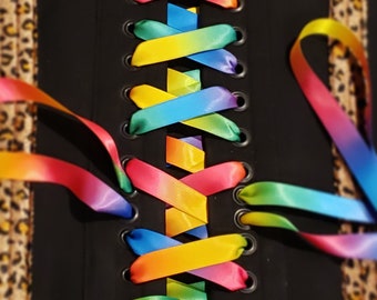May include: A black corset with a leopard print pattern and rainbow ribbon laces. The laces are tied in a criss-cross pattern.