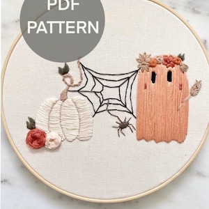 May include: Embroidered hoop art featuring a white pumpkin, a spider web, a spider, and a ghost with a floral crown. The text "PDF PATTERN" is in a circle above the design.