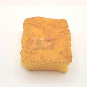 May include: A rectangular, golden-yellow food item with a textured, slightly browned top surface. The edges are uneven and crinkled, and the side profile shows a layered, porous structure. A faint, semi-transparent rectangular logo is visible.