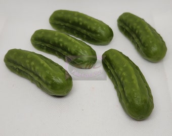 May include: Five green plastic pickle replicas, arranged on a white surface. The pickles are realistic looking and have a bumpy texture.