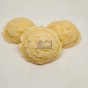 May include: Three scoops of pale yellow ice cream, arranged on a white surface. The scoops have a textured appearance, suggesting a creamy, frozen dessert. The image includes a logo with the text "Fake Food Plus".
