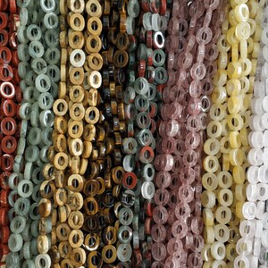 Puede incluir: Surtido de cuentas de piedras preciosas de colores con un agujero en el centro. Las cuentas est&aacute;n enhebradas en filas, creando una pantalla colorida y texturizada.