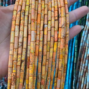 Puede incluir: Una hebra de cuentas de jaspe naranja y amarillo, cada cuenta tiene forma cilíndrica con un patrón de mármol.