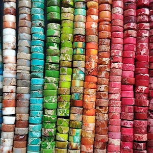 Puede incluir: Una variedad de cuentas redondas y planas de colores, hechas de piedra natural. Las cuentas están dispuestas en filas, con cada fila presentando un color y un patrón diferente. Las cuentas son perfectas para la elaboración de joyas, la artesanía y la decoración del hogar.