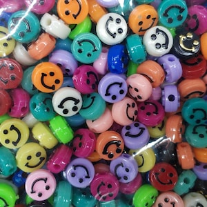 May include: A variety of colorful plastic smiley face beads. The beads are in a variety of colors, including red, blue, green, yellow, and orange. The beads are all about 1 inch in diameter.