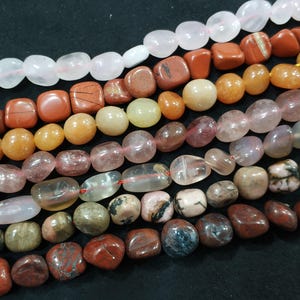 May include: Assortment of gemstone beads in various shapes and colors, including pink, orange, brown, and clear. The beads are strung together, showcasing a variety of textures and natural patterns. Ideal for jewelry making or craft projects.