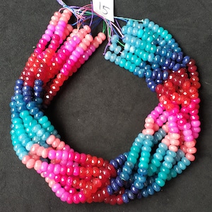 May include: A strand of colorful gemstone beads in shades of pink, red, blue, and turquoise. The beads are faceted and have a slightly irregular shape. The strand is approximately 15 inches long.