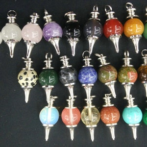May include: A collection of 24 gemstone pendulums with silver-toned metal caps and points. The pendulums are made of various gemstones, including clear, white, pink, purple, black, gray, red, orange, green, blue, brown, and yellow.