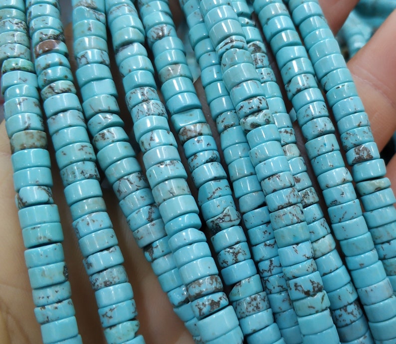 May include: A strand of turquoise beads, each bead is a cylinder with a light blue color and a mottled pattern. The beads are strung together on a clear thread.