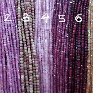 May include: Seven strands of square-shaped gemstone beads in various shades of pink, red, and brown. The beads are strung on a cord and are arranged in a row.