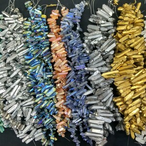 Puede incluir: Surtido de cuentas de cristal de punta iridiscente en varios colores, incluyendo verde, plata, azul, melocotón, morado, gris, oro y blanco. Las cuentas están dispuestas en filas y están listas para ser utilizadas para la elaboración de joyas.
