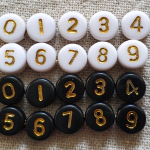 Peut inclure: Deux ensembles de dix perles rondes, blanches et noires avec des chiffres dorés de 0 à 9. Les perles sont disposées en deux rangées de dix, les perles blanches dans la rangée du haut et les perles noires dans la rangée du bas.