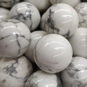 May include: Close-up of a collection of white, spherical stones with grey veining. The polished spheres are smooth and reflective, with a natural, marbled appearance. These stones are likely decorative or used in crafts.