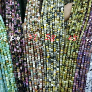 Może przedstawiać: Zbliżenie na różnorodne koraliki z kamieni szlachetnych, w tym akwamaryn, ametyst i zielony awenturyn. Koraliki są wszystkie kwadratowe i nawleczone na sznurek. Liczby 32, 26, 56, 57, 58, 25, 45 i 52 są napisane na sznurkach.