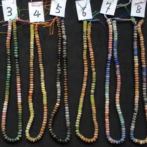 May include: Ten strands of gemstone bead necklaces in various colors, including brown, green, pink, and blue. Each necklace is made of small, round beads and is displayed against a black background. Each strand is labeled with a number.