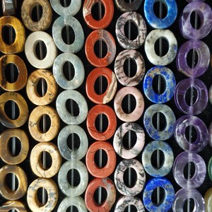 Puede incluir: Una colecci&oacute;n de cuentas de piedra preciosa de color donut con un agujero en el centro. Las cuentas est&aacute;n hechas de varias piedras naturales, incluyendo &aacute;gata, jaspe y amatista.