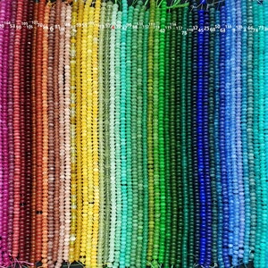 Könnte beinhalten: 47 Stränge runder Edelsteinperlen in verschiedenen Farben, darunter Weiß, Rosa, Rot, Orange, Gelb, Grün, Blau, Lila und Braun. Jeder Strang ist mit einer Nummer von 1 bis 47 gekennzeichnet.