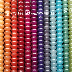May include: A close-up of a row of 15 different coloured beads. The beads are round and smooth, and they range in colour from white to green. The beads are numbered 150 to 159.