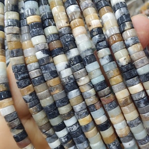May include: A strand of multi-colored gemstone beads. The beads are round and have a mottled appearance, with shades of brown, black, white, and green. The beads are strung on a clear thread.