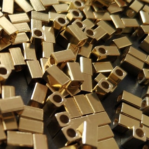 Pode incluir: Um grande monte de peças de conexão de metal de cor dourada. As peças são de forma retangular com um pequeno furo no centro.