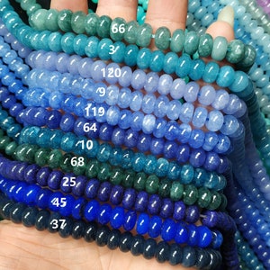 Puede incluir: Una variedad de cuentas de piedras preciosas azules, verdes y moradas, dispuestas en filas por color. Las cuentas son redondas y tienen un acabado liso y pulido. Los números 66, 3, 120, 9, 119, 64, 10, 68, 25, 45 y 37 son visibles en la imagen.