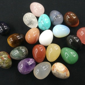 May include: A collection of 18 polished gemstone eggs in various colors and textures, including clear quartz, amethyst, tiger's eye, and rose quartz.
