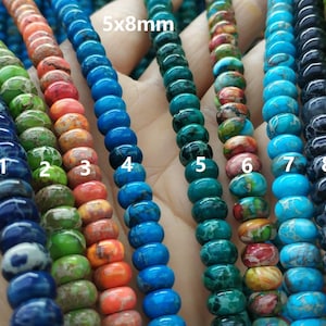 Op de afbeelding: Negen strengen ronde kralen van 5x8 mm in verschillende kleuren, waaronder blauw, groen, oranje en zwart. De kralen hebben een marmerpatroon.