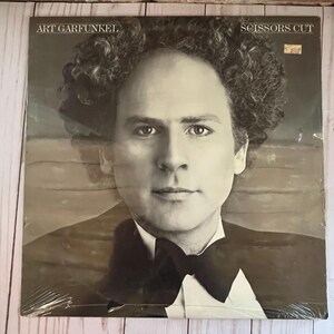 May include: A vinyl record album titled "Scissors Cut" by Art Garfunkel. The album cover features a black and white portrait of Art Garfunkel in a tuxedo. The album is sealed in plastic.