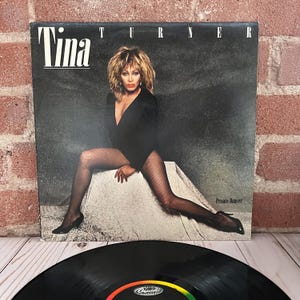 May include: A vinyl record album cover featuring Tina Turner. The album cover has the name "Tina" in large white letters, with "Turner" above the image. Tina is wearing a black outfit and fishnet stockings. The album title "Private Dancer" is also visible.