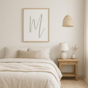 May include: A framed print with the letter "M" in a soft green hue hangs above a bed with neutral-toned bedding. A woven pendant light and a wooden nightstand with a lamp and vase complete the bedroom decor.