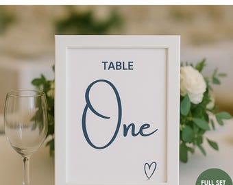 May include: A white framed table number with the word "One" in navy blue script. The text "Printable Wedding Table Numbers 1-20 Instant Download" is at the top. A small heart is at the bottom.