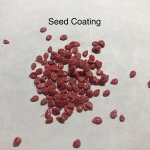 Puede incluir: Primer plano de un mont&oacute;n de recubrimiento de semillas rojo. Las semillas son peque&ntilde;as y redondas, y est&aacute;n recubiertas de un polvo rojo. El texto "Seed Coating" es visible en la parte superior de la imagen.