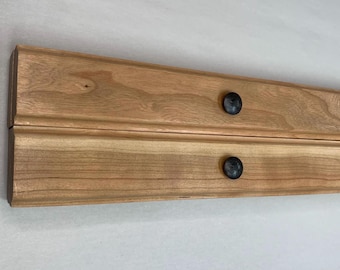 May include: Two pieces of wood with a natural wood finish are joined together with black metal knobs. The wood has a grain pattern.