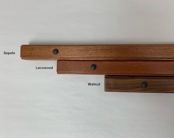 May include: Three wood samples with black metal accents. The wood samples are labeled "Sapele", "Lacewood", and "Walnut".