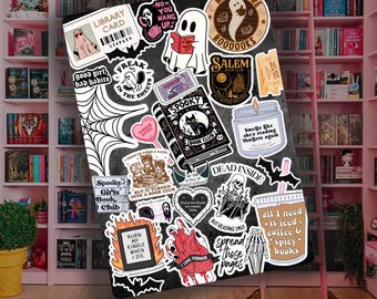 May include: A collection of spooky-themed stickers on a black background, featuring ghosts, books, and phrases like "Spooky Book Club" and "Dead Inside." The stickers are surrounded by a pink bookshelf.