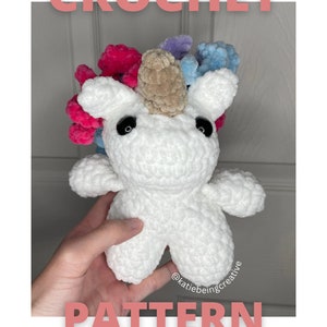 May include: Crochet pattern for a white unicorn amigurumi toy with a pink, blue, and purple mane. The unicorn has black eyes and a brown horn. The pattern is available for download. *NOT a physical item*