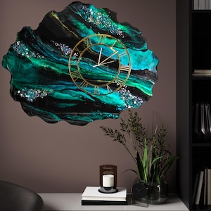 Puede incluir: Un reloj de resina negro, verde y dorado con números romanos. El reloj tiene forma de nube y un diseño abstracto único.