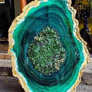May include: A large, round, green and gold resin art piece with a swirling, agate-like pattern. The center of the piece is filled with small, green and gold glitter.